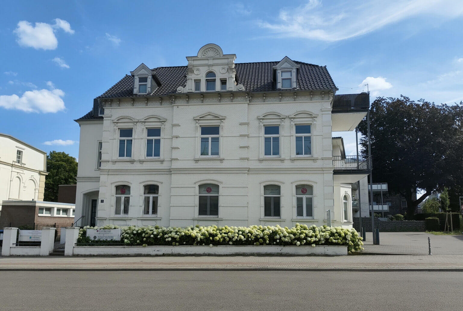 Standort von MKDev: weiße Gründerzeit-Villa mit Hortensienhecke unter blauem Himmel